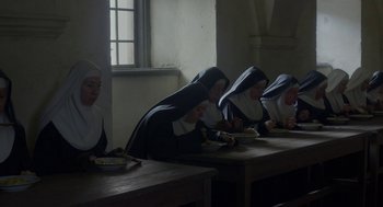 Movie still from “The Innocents” (2016), directed by Anne Fontaine – A group of nuns sitting at a wooden table eating food; Wide shot, High angle
