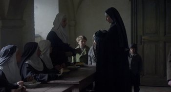 Movie still from “The Innocents” (2016), directed by Anne Fontaine – A group of people sitting around a table; Medium shot, Over the shoulder angle