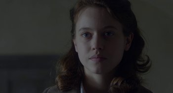 Movie still from “The Innocents” (2016), directed by Anne Fontaine – A young woman with long red hair is looking at the camera; Close Up shot, Over the shoulder angle