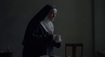 Movie still from “The Innocents” (2016), directed by Anne Fontaine – A nun is holding a coffee mug in a dark room; Medium shot, High angle