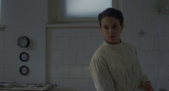 Movie still from “The Innocents” (2016), directed by Anne Fontaine – A person standing next to a window in a room; Medium shot, Over the shoulder angle