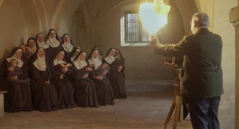 Movie still from “The Innocents” (2016), directed by Anne Fontaine – A group of nuns are sitting in front of a priest; Wide shot, High angle