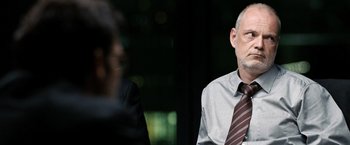 Movie still from “The International” (2009), directed by Tom Tykwer – A man wearing a tie sitting in front of another man; Close Up shot, Over the shoulder angle