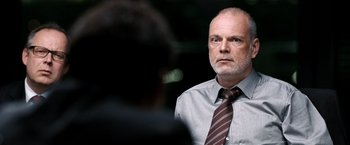 Movie still from “The International” (2009), directed by Tom Tykwer – An older man wearing a shirt and a tie; Close Up shot, Over the shoulder angle