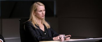 Movie still from “The International” (2009), directed by Tom Tykwer – A woman sitting at a table in front of a glass of water; Close Up shot, Over the shoulder angle