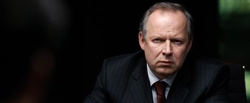 Movie still from “The International” (2009), directed by Tom Tykwer – An older man in a suit and tie looking at the camera; Close Up shot, Low angle