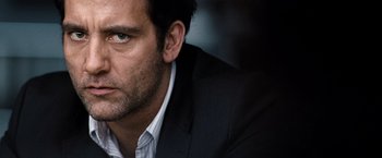 Movie still from “The International” (2009), directed by Tom Tykwer – A person wearing a suit and tie; Close Up shot, Over the shoulder angle