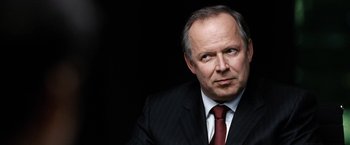 Movie still from “The International” (2009), directed by Tom Tykwer – An older man in a suit and tie looking to his left; Close Up shot, Over the shoulder angle