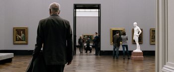 Movie still from “The International” (2009), directed by Tom Tykwer – A group of people standing in a room with paintings on the wall; Medium shot, Over the shoulder angle