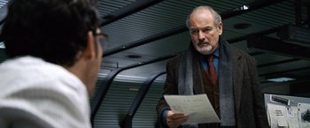 Movie still from “The International” (2009), directed by Tom Tykwer – An older man reading a piece of paper while standing next to another man; Medium shot, Low angle