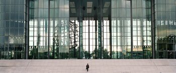 Movie still from “The International” (2009), directed by Tom Tykwer – A person sitting on a set of steps in front of a building; Extreme Wide shot, Low angle