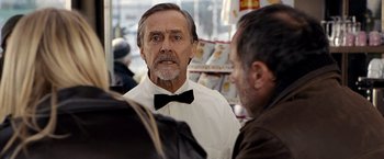 Movie still from “The International” (2009), directed by Tom Tykwer – An older man wearing a white shirt and black bow tie; Close Up shot, Over the shoulder angle