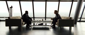 Movie still from “The International” (2009), directed by Tom Tykwer – Two men sitting in front of each other in front of a large window; Wide shot, Over the shoulder angle