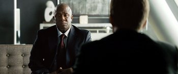 Movie still from “The International” (2009), directed by Tom Tykwer – A man in a suit and tie sitting in front of another man; Close Up shot, Over the shoulder angle