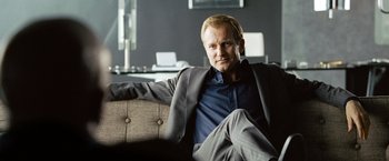 Movie still from “The International” (2009), directed by Tom Tykwer – A man sitting on top of a couch in a room; Close Up shot, Low angle
