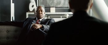 Movie still from “The International” (2009), directed by Tom Tykwer – A man in a suit and tie sitting next to another man in a suit and tie; Close Up shot, Over the shoulder angle