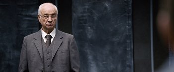 Movie still from “The International” (2009), directed by Tom Tykwer – An older man in a suit and tie; Close Up shot, Over the shoulder angle