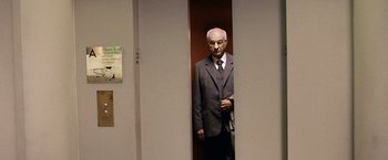 Movie still from “The International” (2009), directed by Tom Tykwer – An older man in a suit standing in front of a door; Medium shot, Low angle