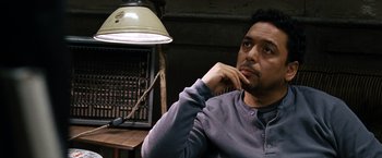 Movie still from “The International” (2009), directed by Tom Tykwer – A man sitting in front of a lamp in a room; Close Up shot, High angle