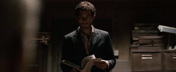 Movie still from “The International” (2009), directed by Tom Tykwer – A man in a suit holding a book in his hands; Medium shot, Low angle
