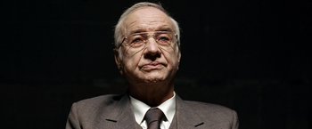 Movie still from “The International” (2009), directed by Tom Tykwer – An older man wearing a suit and tie; Close Up shot, Low angle