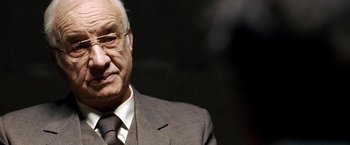 Movie still from “The International” (2009), directed by Tom Tykwer – An older man wearing a suit and tie; Close Up shot, Over the shoulder angle