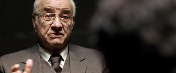 Movie still from “The International” (2009), directed by Tom Tykwer – An older man wearing a suit and tie; Close Up shot, Over the shoulder angle