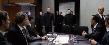 Movie still from “The International” (2009), directed by Tom Tykwer – A group of men standing around a table in a room; Wide shot, Over the shoulder angle