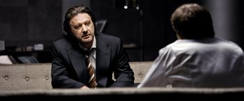 Movie still from “The International” (2009), directed by Tom Tykwer – A man wearing a suit and tie sitting in front of another man wearing a suit; Close Up shot, Over the shoulder angle