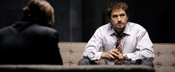 Movie still from “The International” (2009), directed by Tom Tykwer – A man sitting on top of a couch next to a woman; Close Up shot, Over the shoulder angle