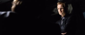 Movie still from “The International” (2009), directed by Tom Tykwer – A man standing in front of a black background; Close Up shot, Over the shoulder angle