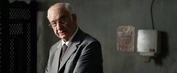 Movie still from “The International” (2009), directed by Tom Tykwer – An older man in a suit and tie; Close Up shot, Over the shoulder angle