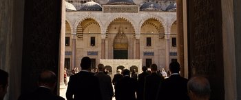 Movie still from “The International” (2009), directed by Tom Tykwer – A group of people standing in front of a large building; Extreme Wide shot, Low angle