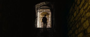Movie still from “The International” (2009), directed by Tom Tykwer – A man standing on some steps in front of an open gate; Extreme Wide shot, Low angle