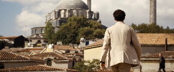 Movie still from “The International” (2009), directed by Tom Tykwer – A man in a white jacket is walking in front of a building; Wide shot, Low angle