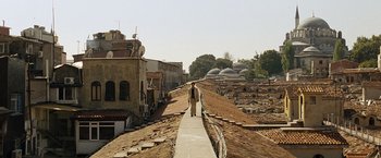 Movie still from “The International” (2009), directed by Tom Tykwer – A man walking down a dirt road near a building; Extreme Wide shot, High angle