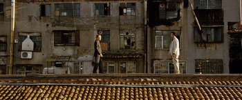 Movie still from “The International” (2009), directed by Tom Tykwer – A man standing on a roof top in front of a building; Extreme Wide shot, Low angle