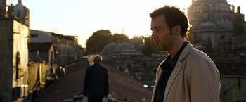 Movie still from “The International” (2009), directed by Tom Tykwer – A man standing next to another man on a dirt road; Medium shot, Low angle