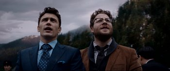 Movie still from “The Interview” (2014), directed by Evan Goldberg – Two men standing next to each other in front of a forest; Medium shot, Low angle