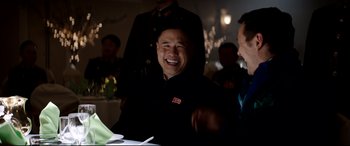 Movie still from “The Interview” (2014), directed by Evan Goldberg – A man laughing while sitting at a dinner table; Medium shot, Over the shoulder angle