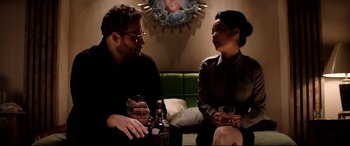 Movie still from “The Interview” (2014), directed by Evan Goldberg – A man and a woman sitting next to each other holding drinks; Medium shot, Over the shoulder angle