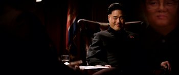 Movie still from “The Interview” (2014), directed by Evan Goldberg – A man sitting at a table in front of an american flag; Medium shot, Low angle