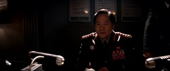 Movie still from “The Interview” (2014), directed by Evan Goldberg – A man in uniform sitting in front of a microphone in a dark room; Medium shot, Over the shoulder angle