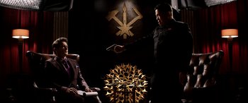 Movie still from “The Interview” (2014), directed by Evan Goldberg – A man in a black suit is holding a gun; Medium shot, Over the shoulder angle