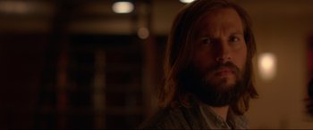 Movie still from “The Invitation” (2015), directed by Karyn Kusama – A man with long hair and a beard is looking at the camera; Close Up shot, Over the shoulder angle