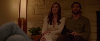Movie still from “The Invitation” (2015), directed by Karyn Kusama – A beautiful woman sitting on a couch next to a potted plant; Medium shot, Over the shoulder angle