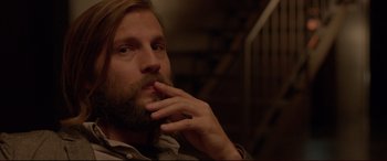 Movie still from “The Invitation” (2015), directed by Karyn Kusama – A man with long hair and a goatee is smoking a cigarette; Close Up shot, Over the shoulder angle