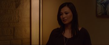 Movie still from “The Invitation” (2015), directed by Karyn Kusama – A woman with long black hair wearing a black shirt; Close Up shot, Over the shoulder angle