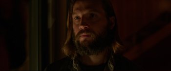 Movie still from “The Invitation” (2015), directed by Karyn Kusama – A man with long hair and a beard looking to his left; Close Up shot, Over the shoulder angle