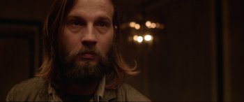 Movie still from “The Invitation” (2015), directed by Karyn Kusama – A man with long hair and a goatee is looking at the camera; Close Up shot, Over the shoulder angle